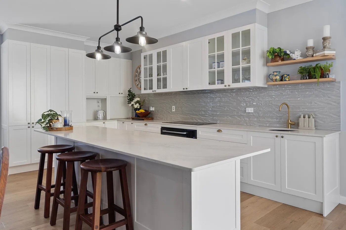 White shaker kitchen with island, grey tiled splashback and brass tapware.