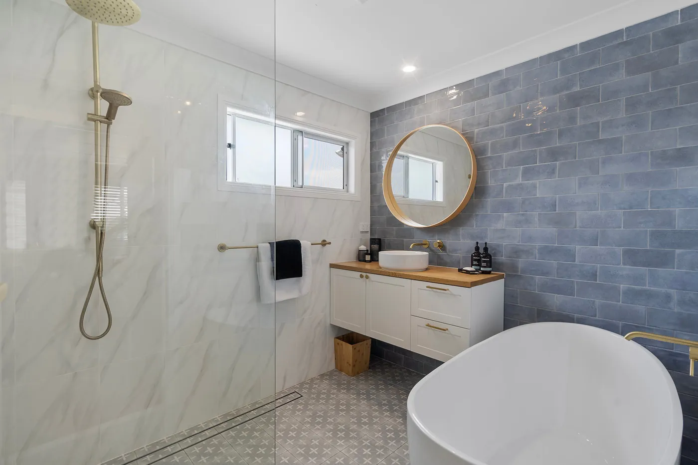 Bathroom with blue feature tiles, timber-topped vanity, round mirror and brass shower fittings.