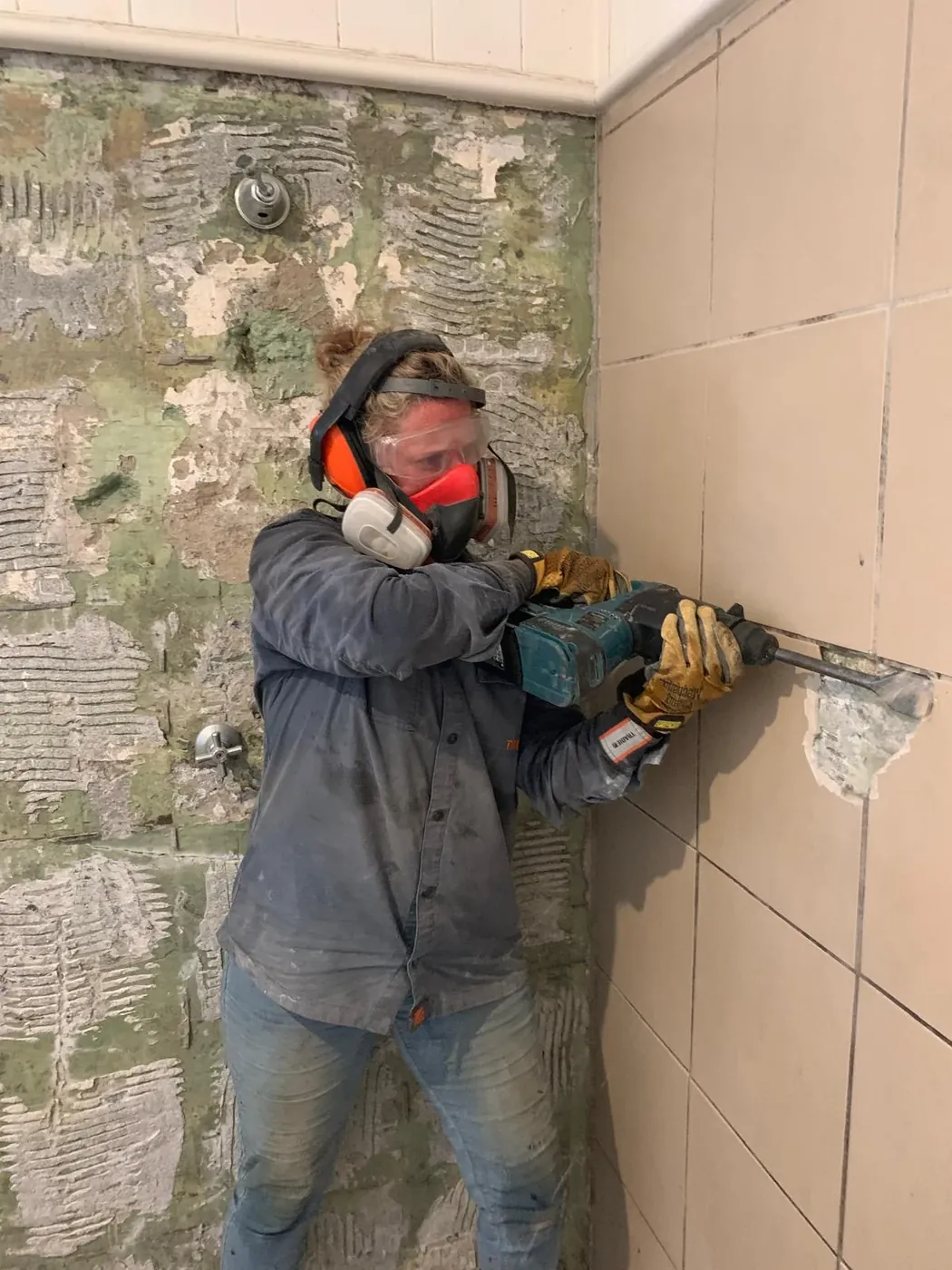 Stacey removing bathroom wall tiles while wearing protective equipment.